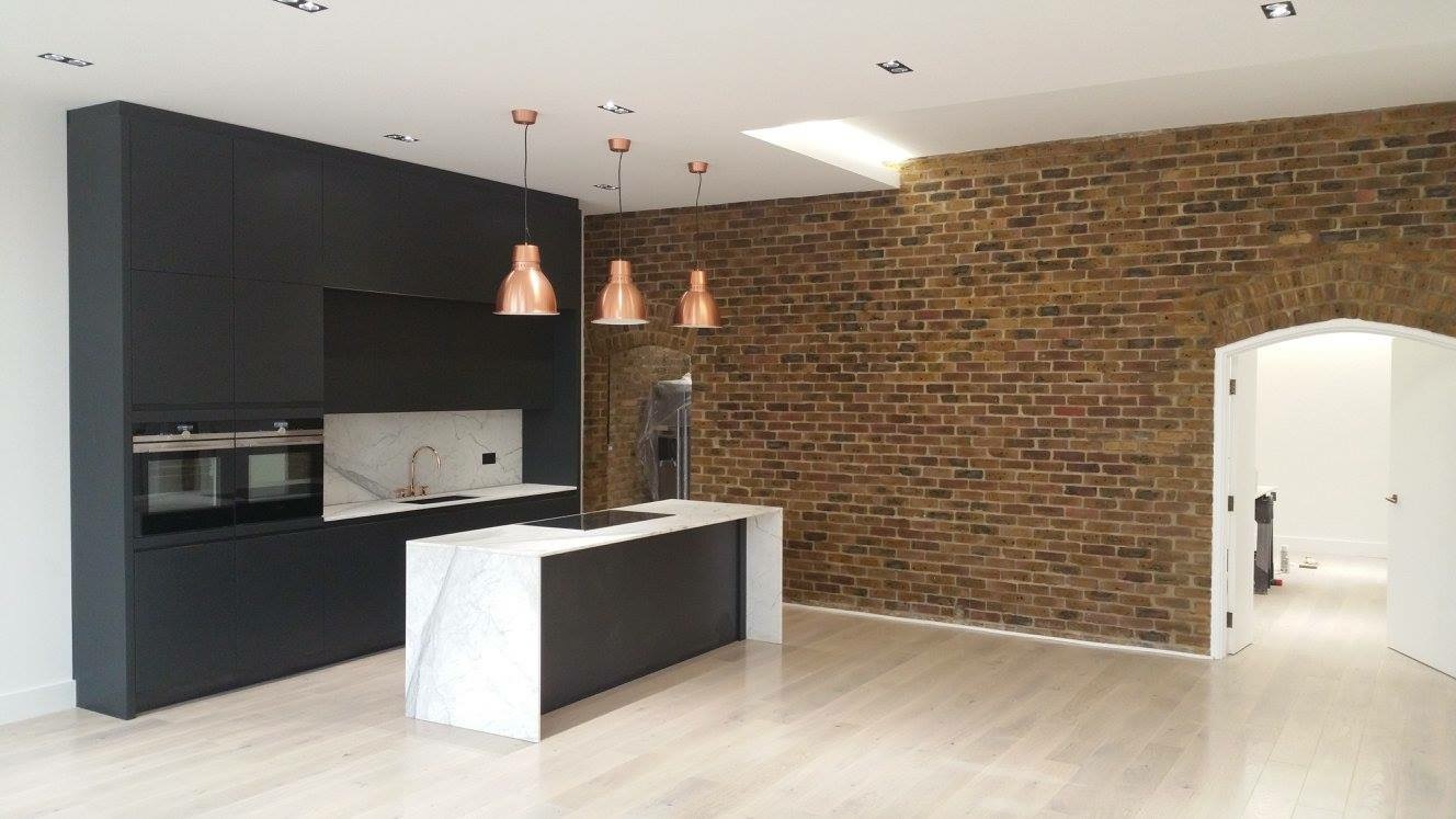 Contemporary kitchen with matt black cabinetry, marble island, copper pendants and exposed brick wall