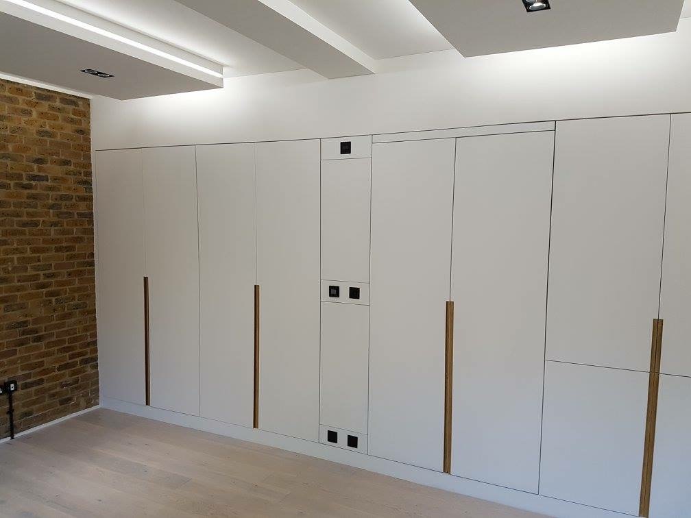 Bespoke floor-to-ceiling fitted wardrobes with oak handles beside an exposed brick wall